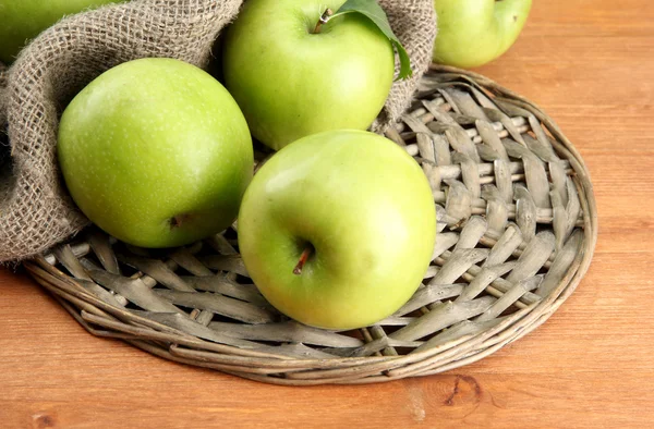 Ripe green apples with leaves on burlap, on wooden table — Stock Photo, Image