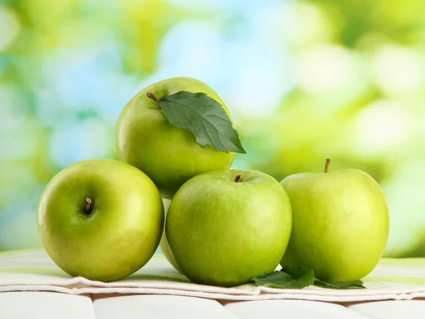 Reife grüne Äpfel mit Blättern, auf Holztisch, auf grünem Hintergrund — Stockfoto