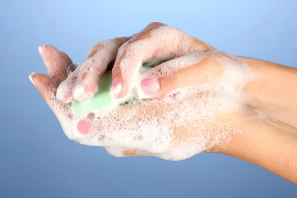 Tangan wanita di soapsuds, di latar belakang biru close-up — Stok Foto