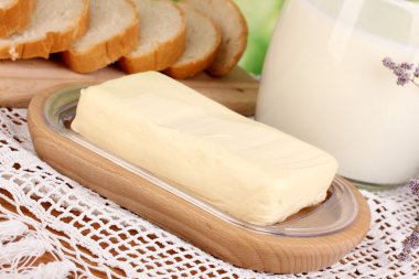 Doğal arka planda ekmek ve sütle çevrili ahşap tutacağa tereyağı.