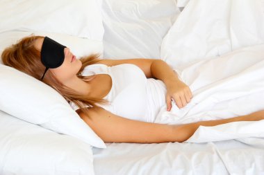Genç ve güzel bir kadın göz maskesiyle yatakta uyuyor.