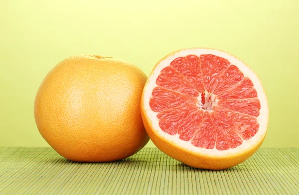 Rijp grapefruit en de helft op bamboe mat op groene achtergrond — Stockfoto