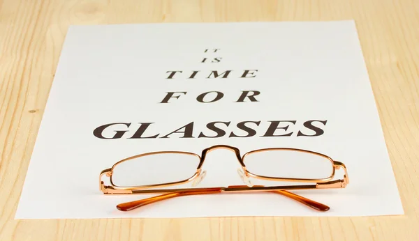 Eyesight test chart with glasses on wooden background close-up — Stock Photo, Image