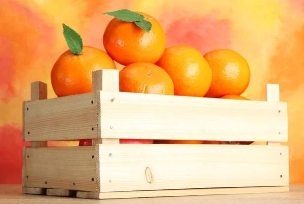 Ripe tasty tangerines with leaves in wooden box on table on orange background — Stock Photo, Image