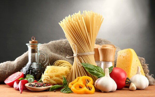 Pasta spaghetti, vegetables and spices, on wooden table, on grey background