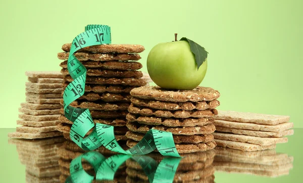 Tasty crispbread, apple and measuring tape, on green background — Stock Photo, Image