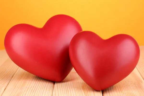 Декоративные красные сердца на деревянном столе на оранжевом фоне — стоковое фото