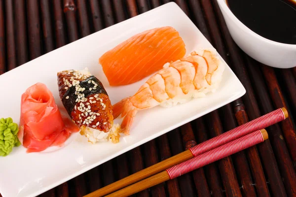 Delicious sushi served on plate on bamboo mat — Stock Photo, Image