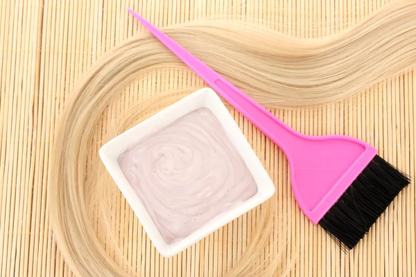 Tintura de cabelo na tigela e escova para coloração de cabelo no tapete de bambu bege, close-up — Fotografia de Stock