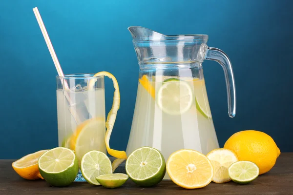 Limonada cítrica en jarra y vaso de cítricos alrededor en mesa de madera en bl —  Fotos de Stock