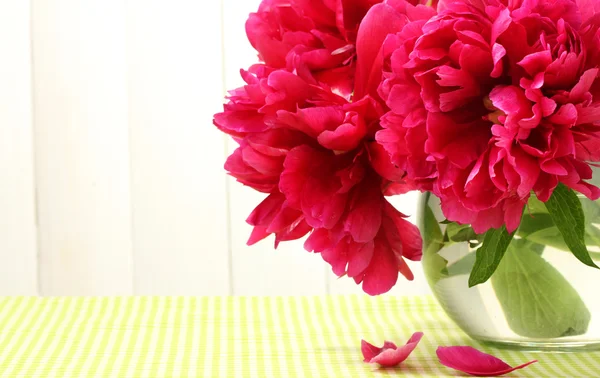白い木製の背景にテーブルの上のガラスの花瓶に美しいピンクの牡丹 — ストック写真