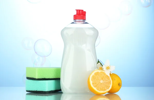 Dishwashing liquid with sponges and lemon with flowers on blue background — Stock Photo, Image