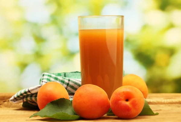 Glas Aprikosensaft und frische Aprikosen auf Holztisch auf grünem Hintergrund — Stockfoto