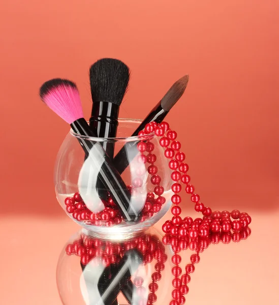 Make-up ecset, egy tál gyöngy nyaklánc, piros háttér — Stock Fotó