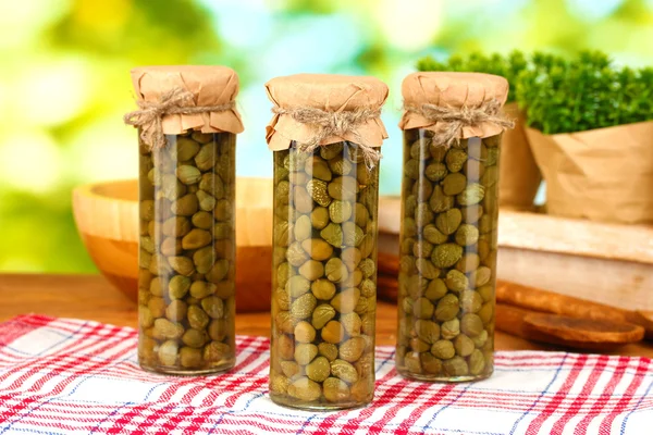 Glass jars with tinned capers on green background — Stock Photo, Image
