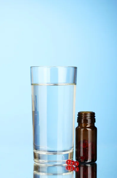 Un bicchiere d'acqua e pillole su sfondo blu primo piano — Foto Stock