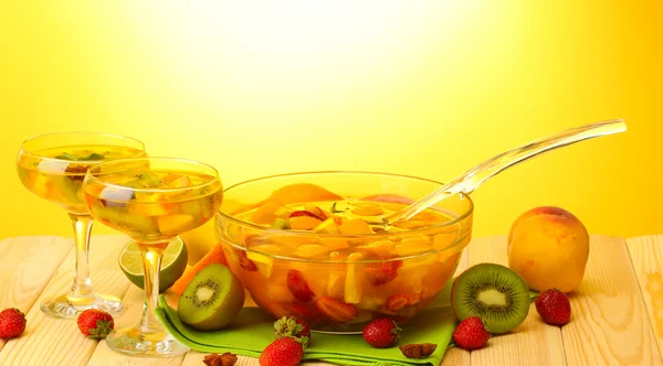 Punch in bowl and glasses with fruits, on wooden table, on yellow backgroun — Stock Photo, Image