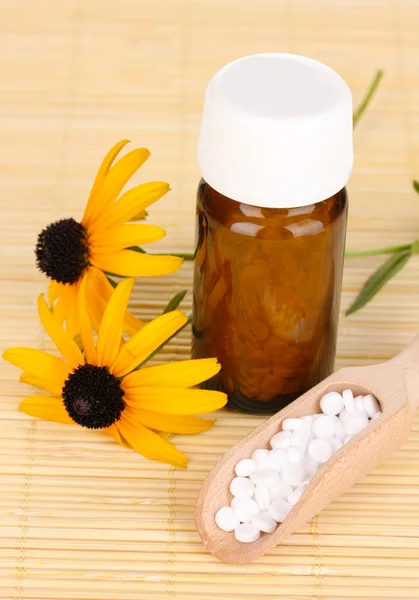 Flacone di medicinale con compresse e fiori su tappetino di bambù — Foto Stock