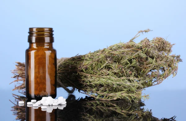 Garrafa com comprimidos e ervas em fundo azul. conceito de homeopatia — Fotografia de Stock