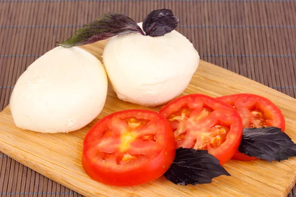 Sabrosa mozzarella con tomates en la tabla de cortar en la estera —  Fotos de Stock