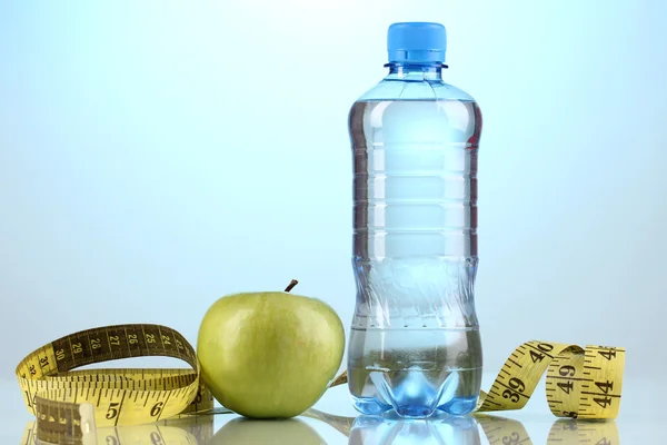 Garrafa de água, maçã e fita métrica em fundo azul — Fotografia de Stock