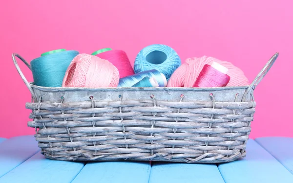 Hilos brillantes en cesta sobre mesa de madera sobre fondo rosa —  Fotos de Stock