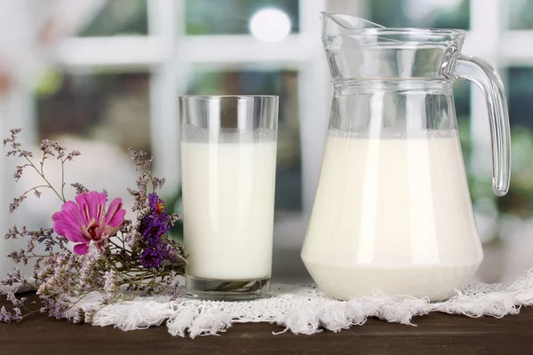 Pitcher and glass of milk on wooden table on window background — Stock Photo, Image