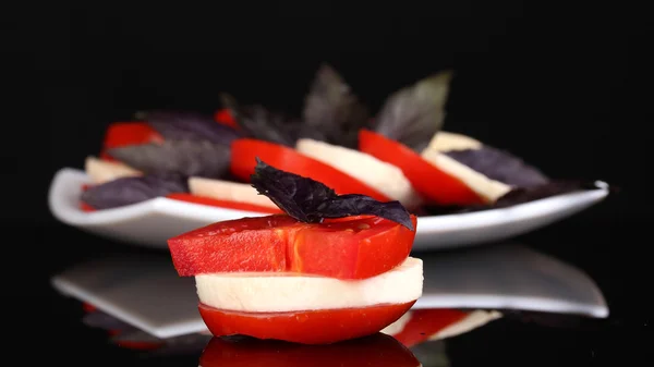 Gustosa mozzarella con pomodori su piatto isolato su nero — Foto Stock