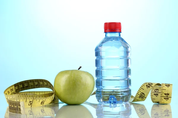 Flaska vatten, apple och måttband på blå bakgrund — Stockfoto