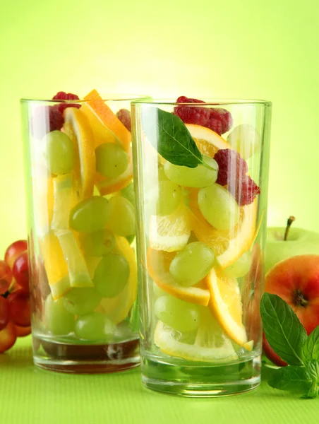 Transparent glasses with citrus fruits, on grren background — Stock Photo, Image