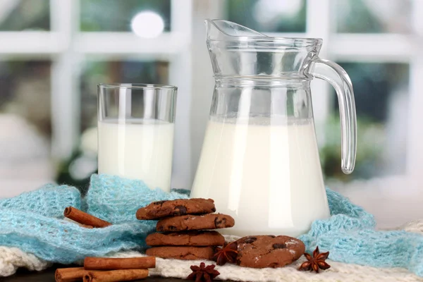 Krug und Glas Milch mit Keksen auf Strickwaren auf hölzernem Tisch — Stockfoto