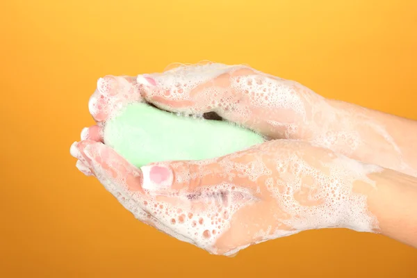 Woman's hands in soapsuds, on orange background close-up — Stock Photo, Image