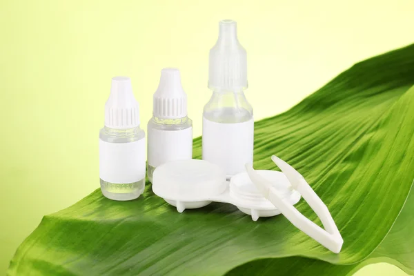 Eye drops and lenses on leaf on green background — Stock Photo, Image