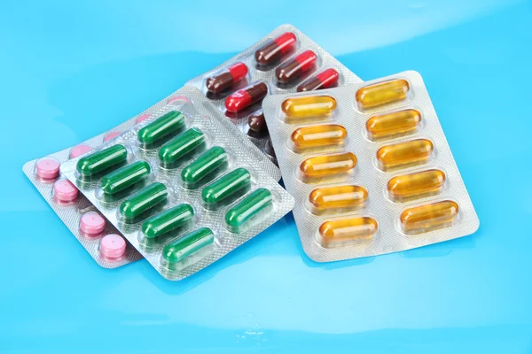 Cápsulas y pastillas empaquetadas en ampollas, sobre fondo azul — Foto de Stock