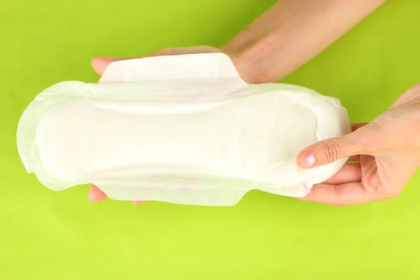 Woman's hands holding a sanitary pad on green background close-up — Stock Photo, Image