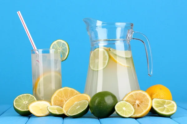 Limonada cítrica en jarra y vaso de cítricos alrededor en mesa de madera en bl —  Fotos de Stock