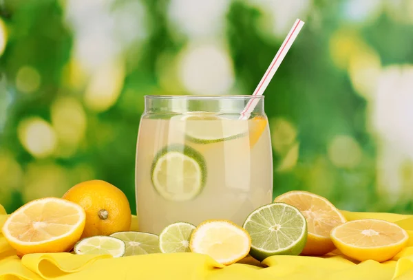 La limonada cítrica en el banco de cristal de los agrios alrededor sobre la tela amarilla sobre natural — Foto de Stock