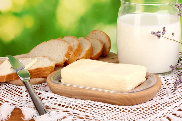 Масло на деревянном держателе в окружении хлеба и молока на естественном фоне — стоковое фото