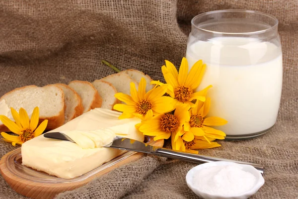 Butter on wooden holder surrounded by bread and milk on sacking background — Stock Photo, Image