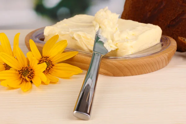 Butter on wooden holder and bread on wooden table on window background — Stock Photo, Image