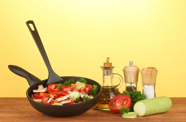 Frying pan with vegetables on yellow background — Stock Photo, Image