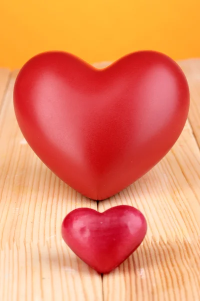 Corações vermelhos decorativos na mesa de madeira no fundo laranja — Fotografia de Stock