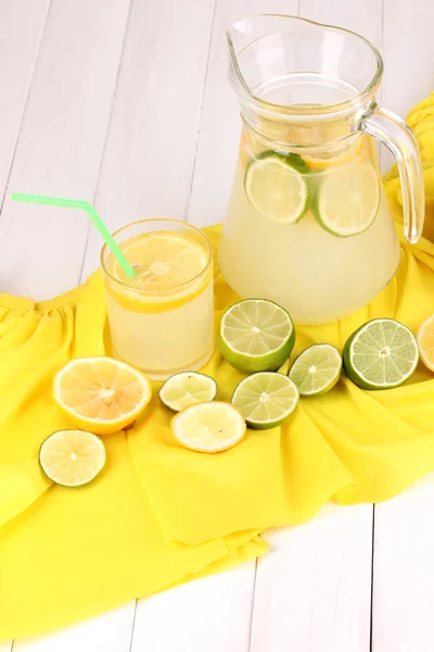 Citrus lemonade in glass and pitcher of citrus around on yellow fabric on w — Stock Photo, Image