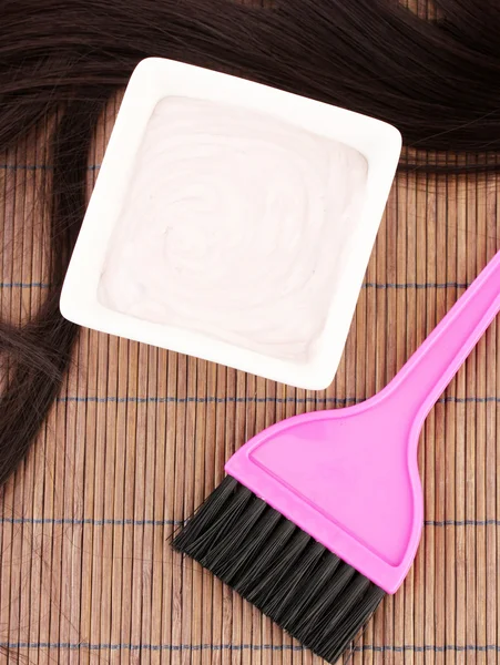Tinte para el cabello en el tazón y el cepillo para la coloración del cabello en la estera de bambú marrón, primer plano —  Fotos de Stock