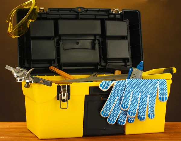 Open yellow tool box with tools on brown background close-up — Stock Photo, Image