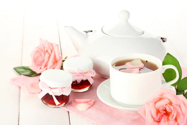 Tetera y taza de té con rosas y mermelada sobre mesa de madera blanca — Foto de Stock