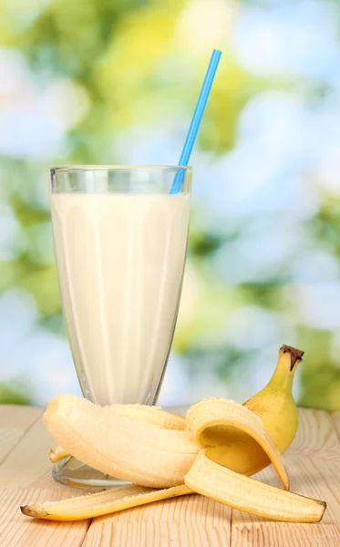 Batido de leite de banana na mesa de madeira no fundo brilhante — Fotografia de Stock