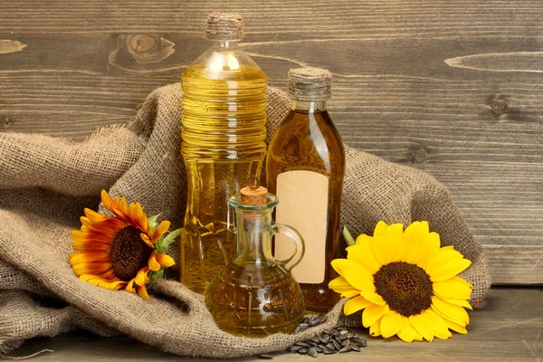 Oil in bottles, sunflowers and seeds, on wooden background — Stock Photo, Image