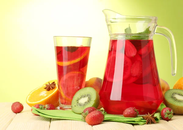 Sangria in jar and glass with fruits, on wooden table, on green background — Stock Photo, Image