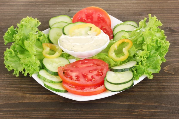 Chopped vegetables and sauce on plate on wooden table — Stock Photo, Image